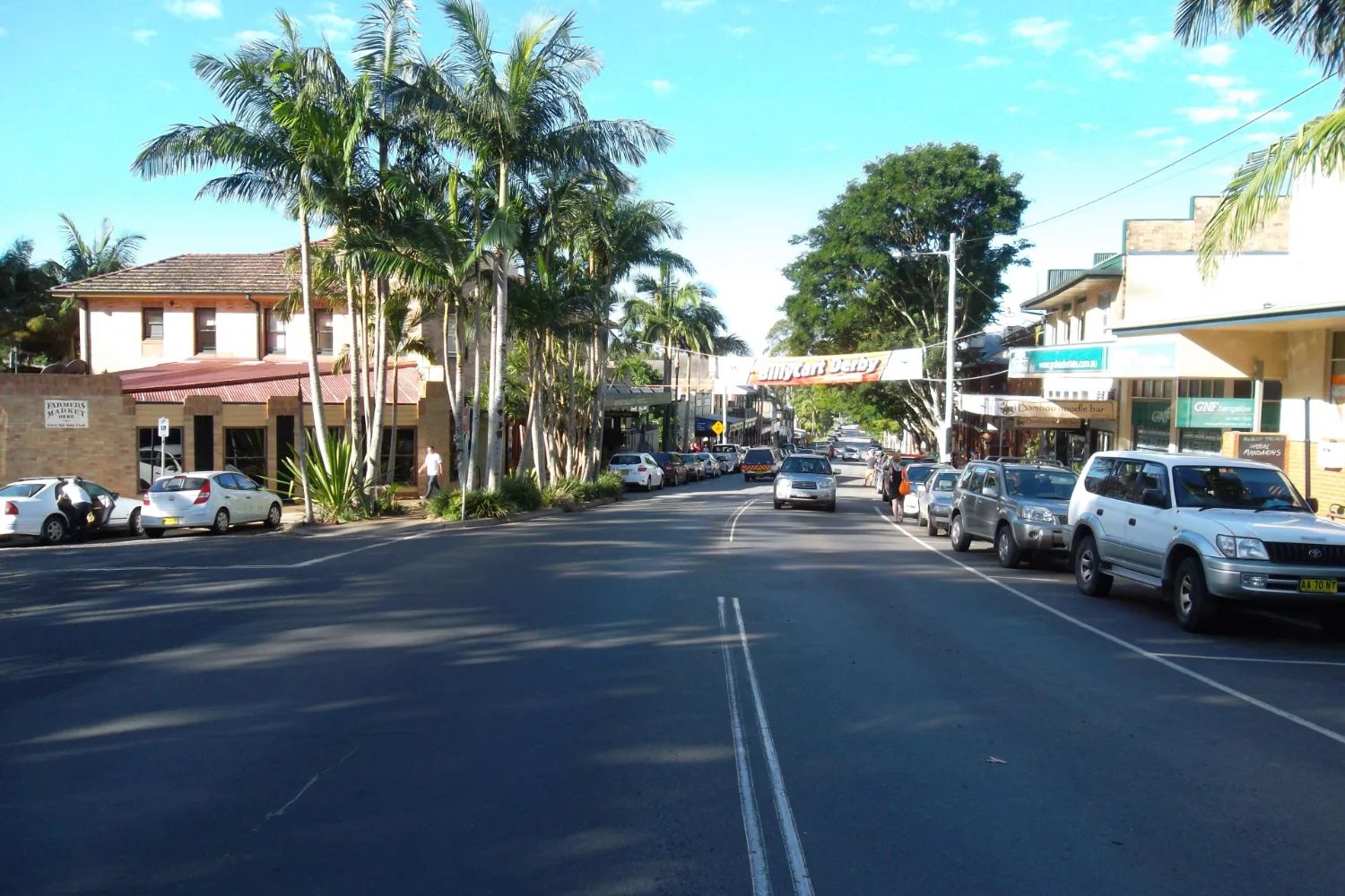 Byron Street, Bangalow's main street, with palm trees, parked cars and shopfronts with verandas