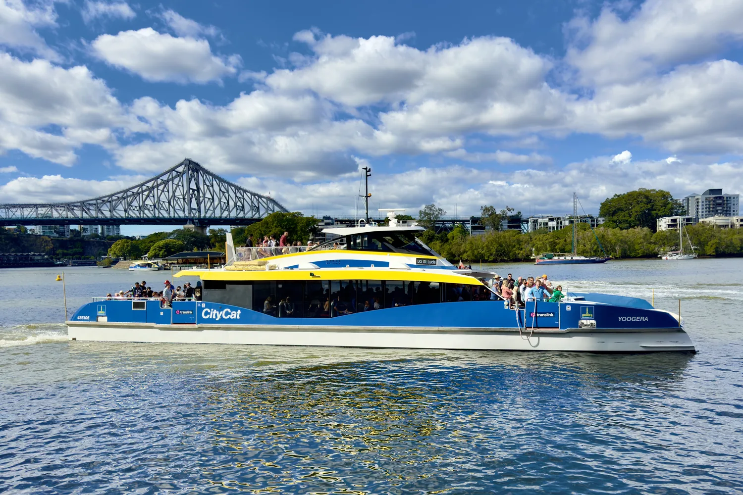 A CityCat ferry on the Brisbane River passing under a bridge, with city towers behind