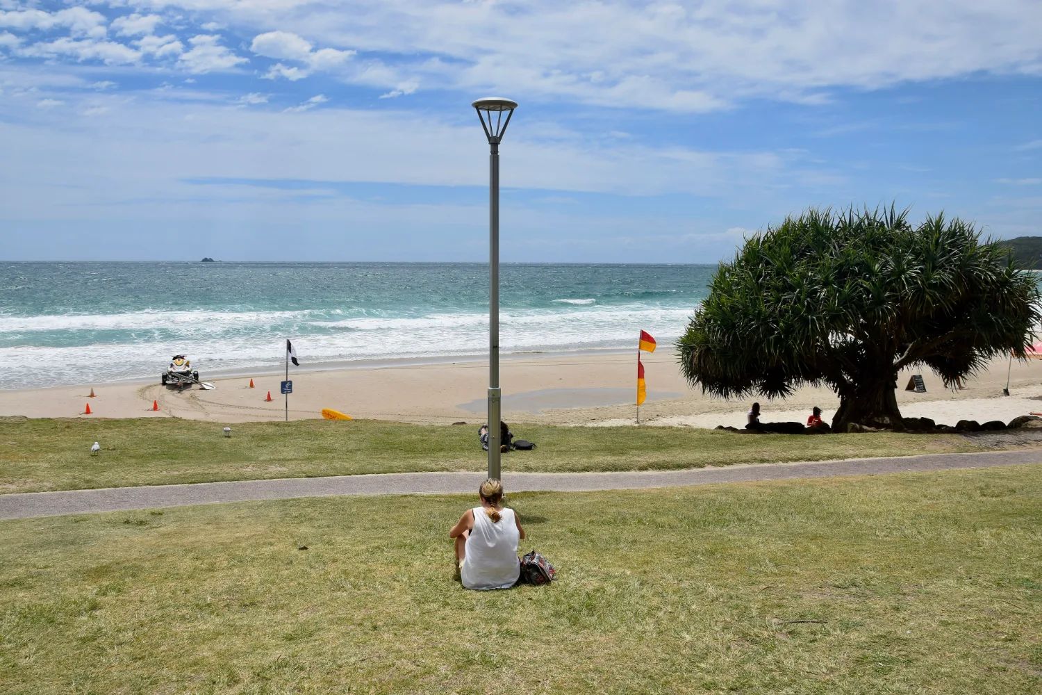 The grassy foreshore at Main Beach, Byron Bay, with people on the sand and surf rolling in