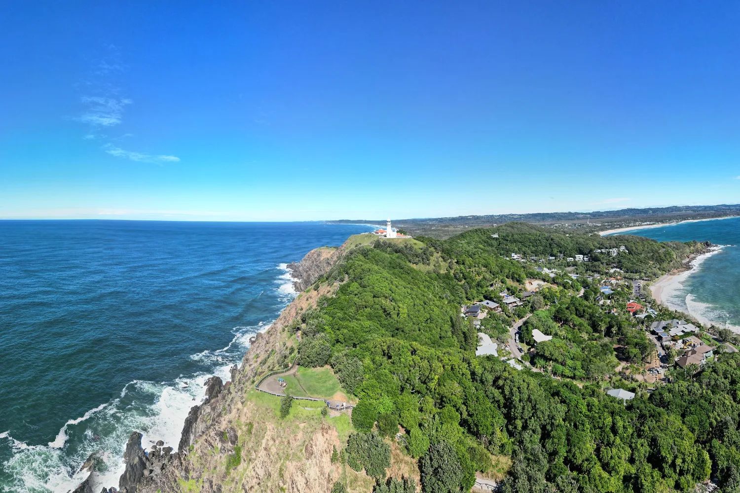 The wooded Cape Byron headland from above, with the lighthouse on its tip and small beaches along its shore