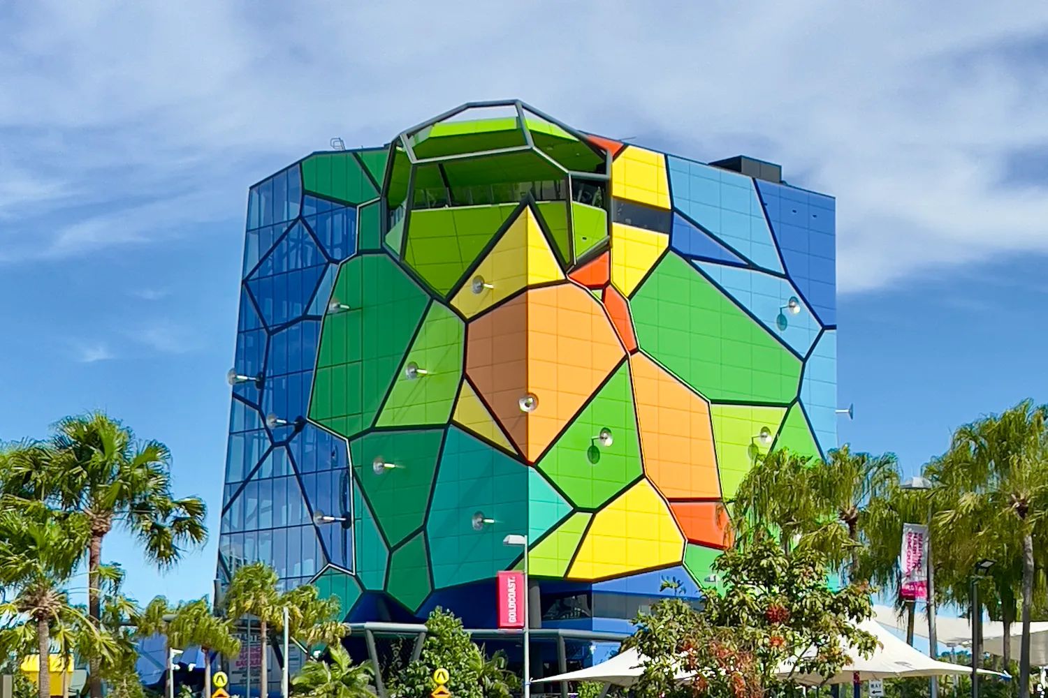 The HOTA Gallery, a tall block clad in a patchwork of green, yellow, orange and blue panels, rising behind palm trees