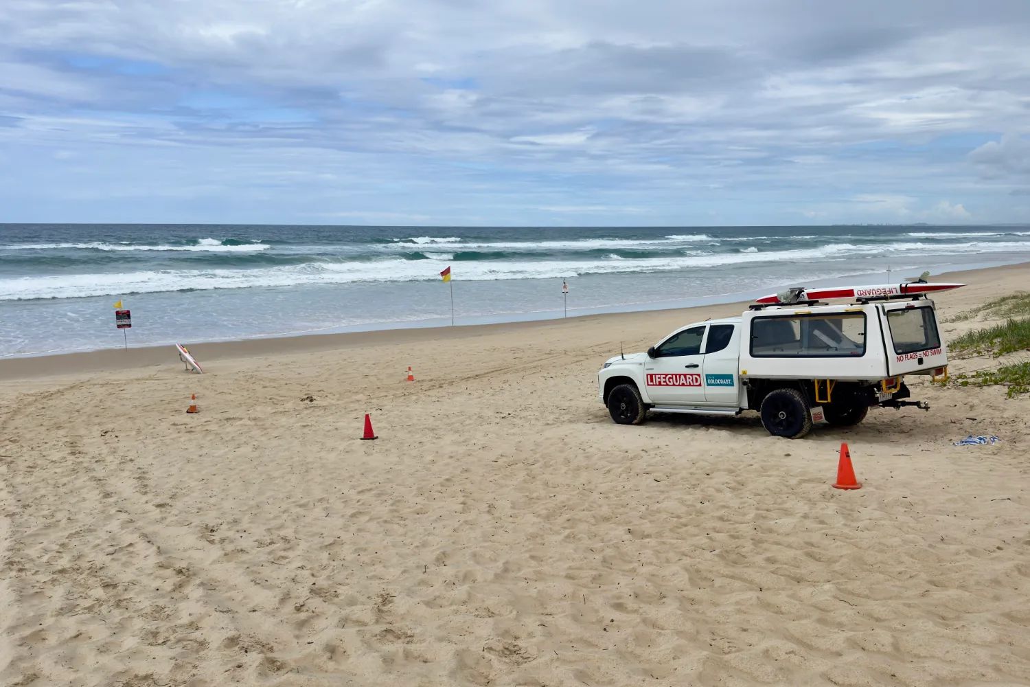A lifeguard’s four-wheel drive parked on the wide sand of The Spit beach, with surf rolling in under a grey sky