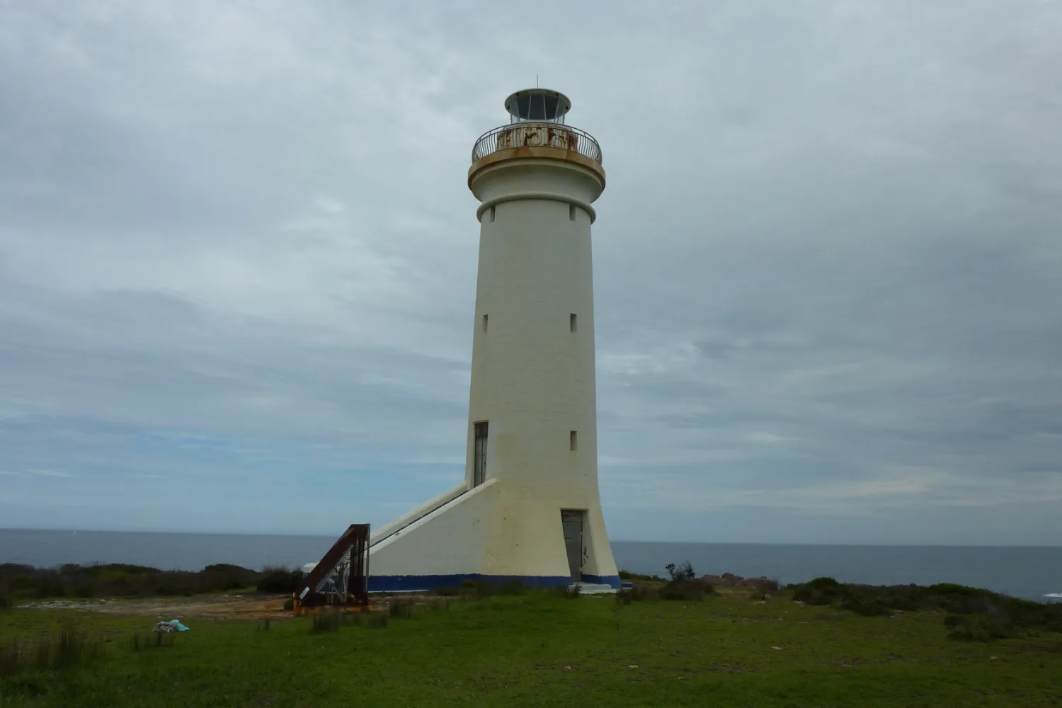 The white tower of the Point Stephens lighthouse on Fingal Island under a grey sky
