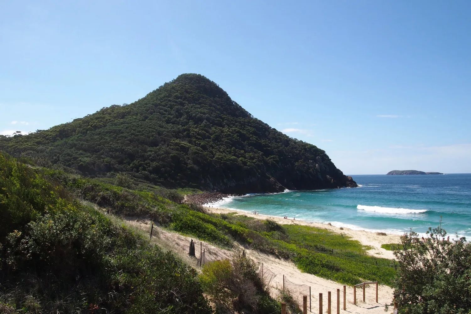 Zenith Beach below the green cone of Tomaree Head, with a sandy track through the scrub down to the surf