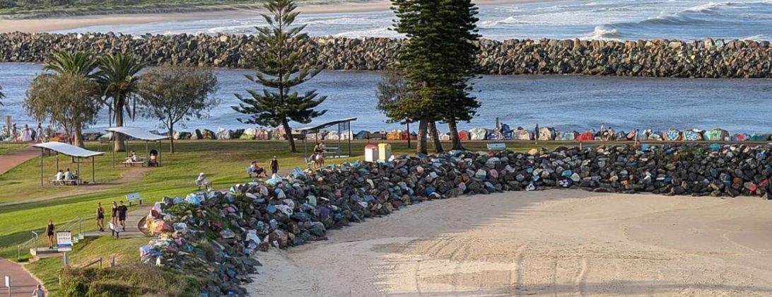 The breakwall at the mouth of the Hastings River in Port Macquarie, with Norfolk pines and a grassy foreshore
