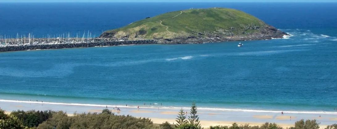 Muttonbird Island seen from the shore, a low green island at the end of the Coffs Harbour breakwall