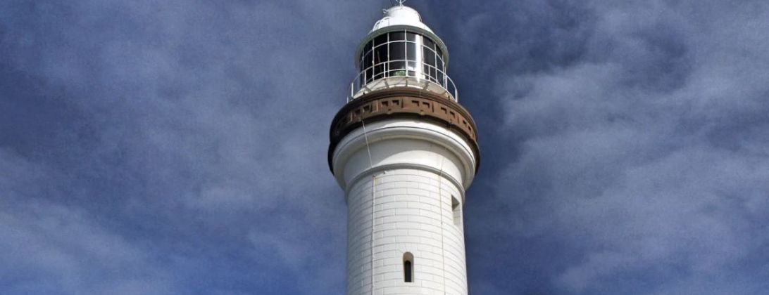 The top of the white Cape Byron lighthouse against a stormy sky