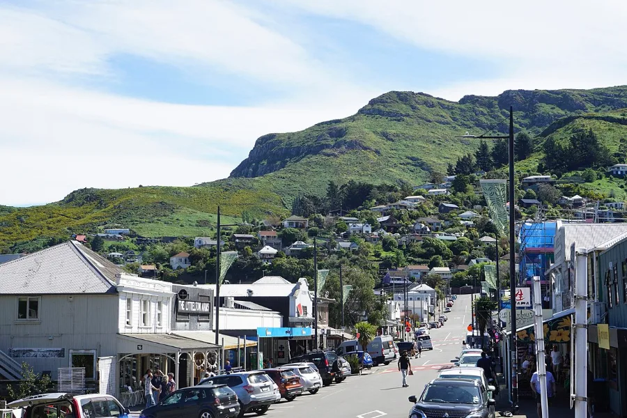 A street of shops in Lyttelton, with the green crater rim of the Port Hills rising behind.
