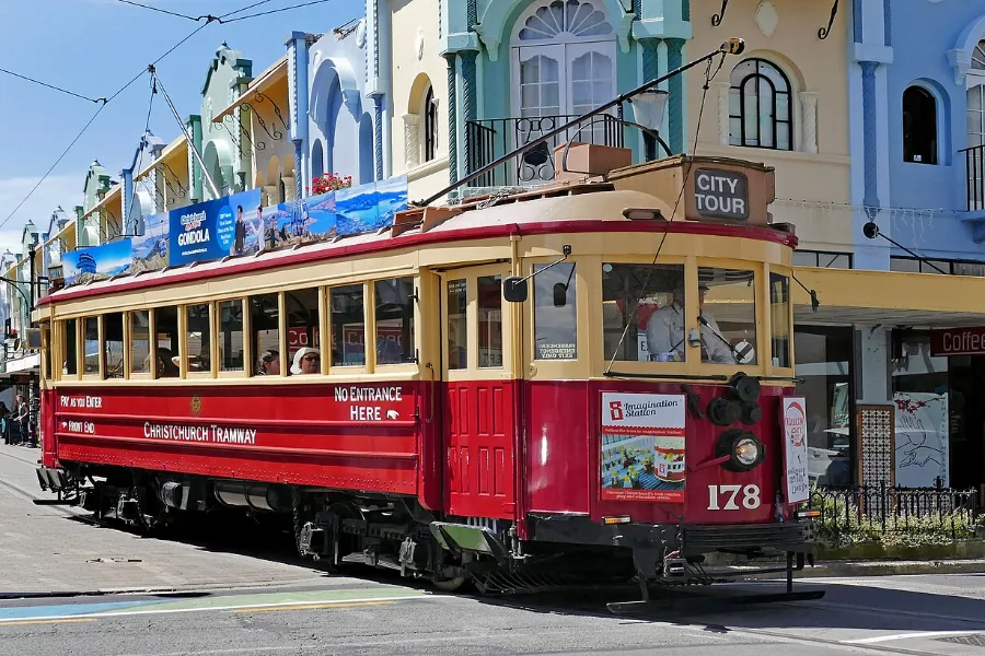 A red and cream heritage tram in New Regent Street, in front of a row of pastel Spanish Mission shopfronts.