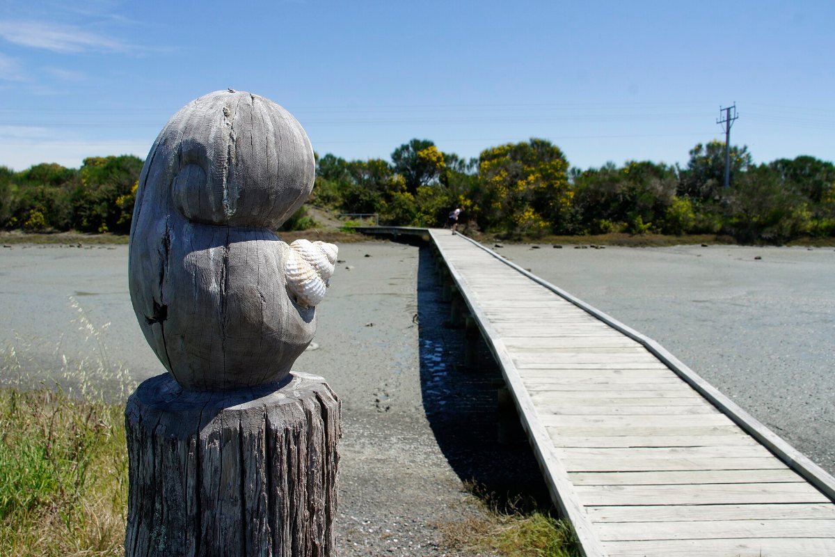 A carved post and a boardwalk path crossing the Ahuriri Estuary in Napier.