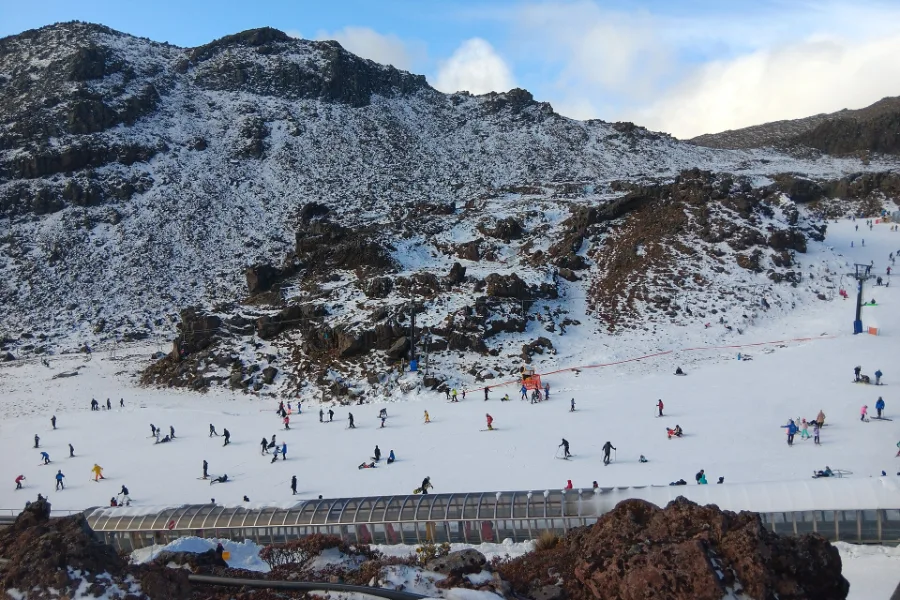 Skiers and snowboarders on the gentle slopes of Happy Valley at Whakapapa, below dark volcanic ridges dusted with snow.