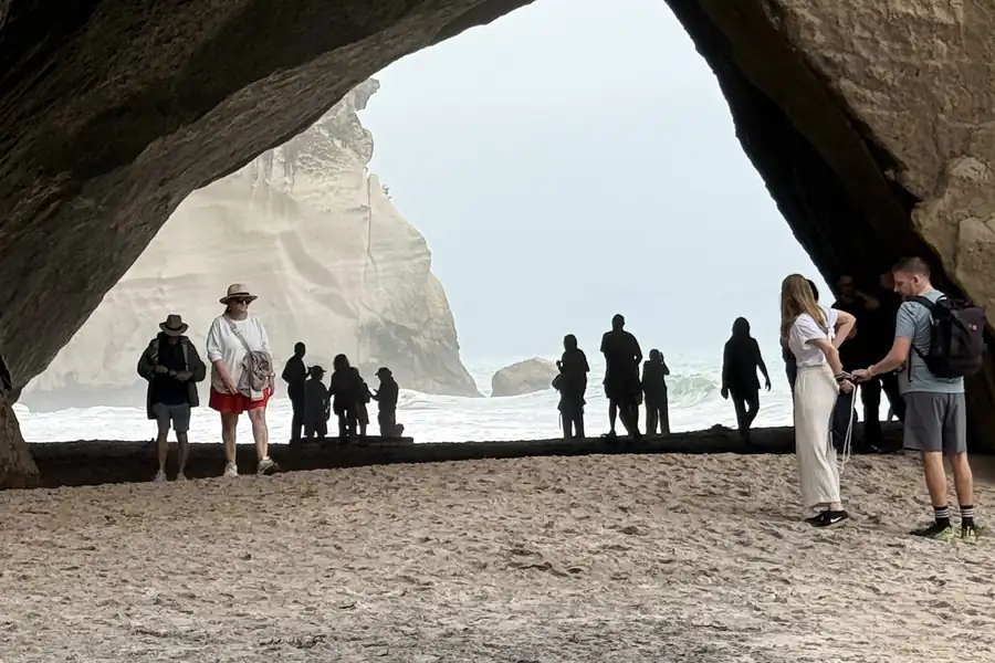 Visitors standing inside the rock arch at Cathedral Cove, with the white cliffs and the sea beyond the opening.