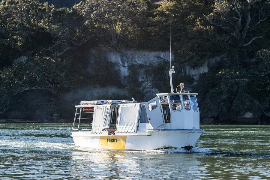 The small Whitianga passenger ferry crossing the harbour mouth, with houses along the far shore.