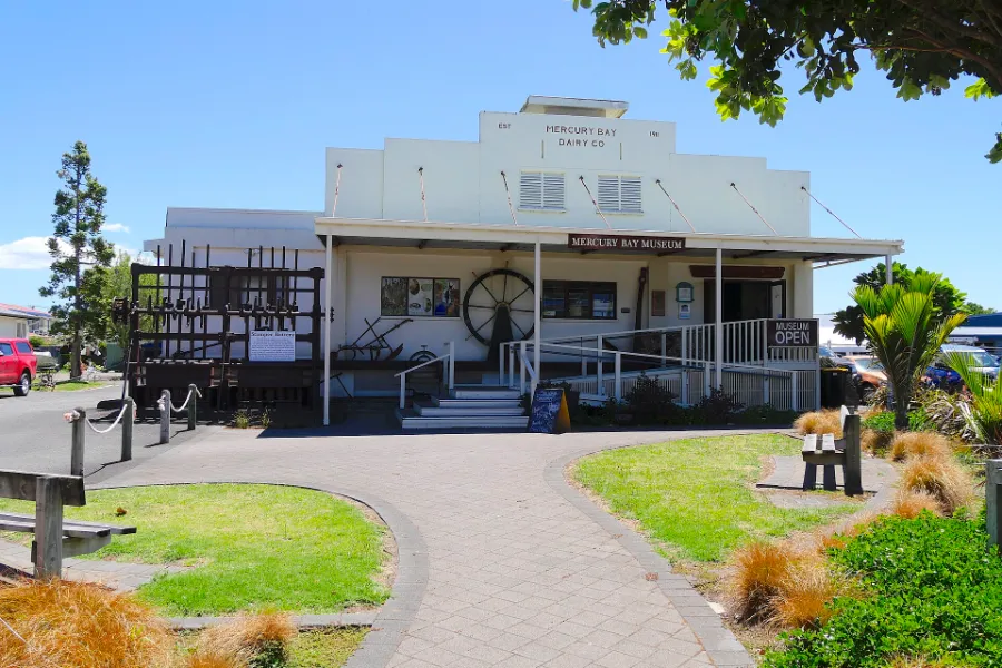The Mercury Bay Museum in Whitianga, a white single-storey former dairy factory with a veranda, facing the road opposite the wharf.