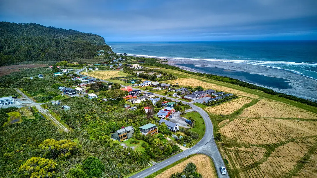 The small settlement of Okarito seen from the air, a scatter of houses between rainforest, a lagoon and a long surf beach.
