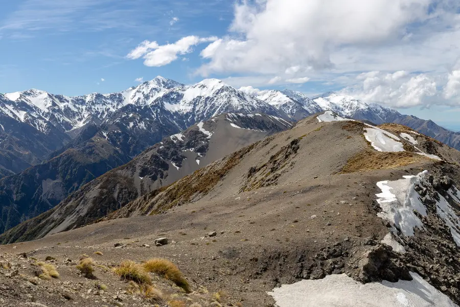 View from high on Mt Fyffe across bare ridges and snow patches to the jagged peaks of the Kaikōura Ranges.