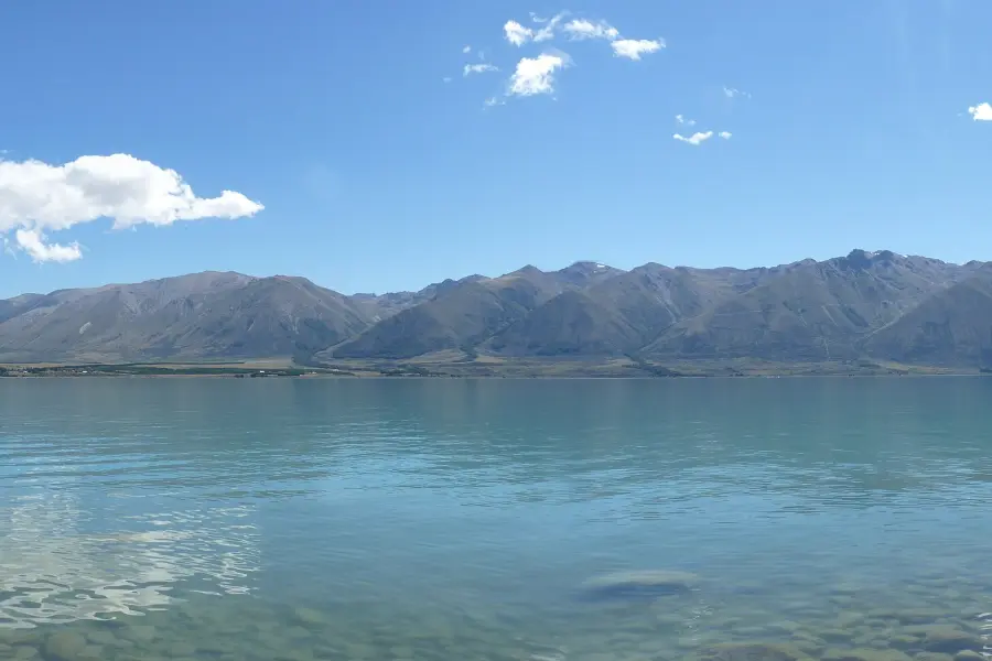 The calm blue water of Lake Ōhau stretching to a line of distant mountains under a clear sky.