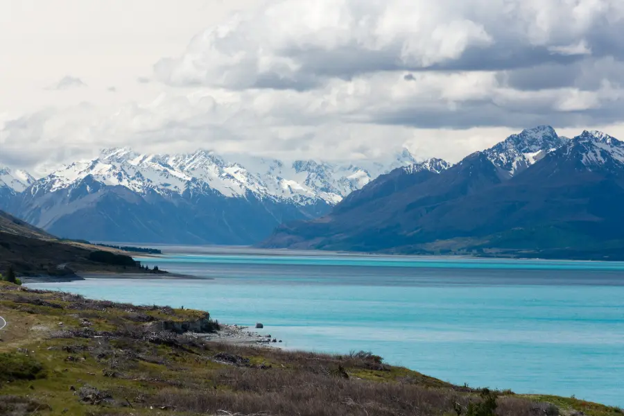 Lake Pūkaki stretching towards Aoraki / Mount Cook and the snow-covered Southern Alps, with the road curving along its shore.