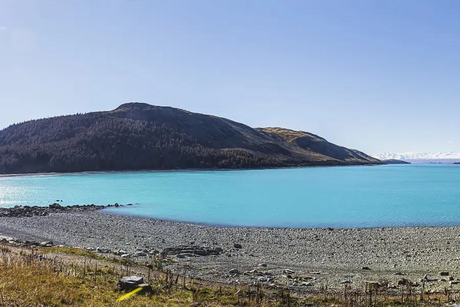 The milky turquoise water of Lake Tekapo under a clear sky, with brown hills along its far shore.