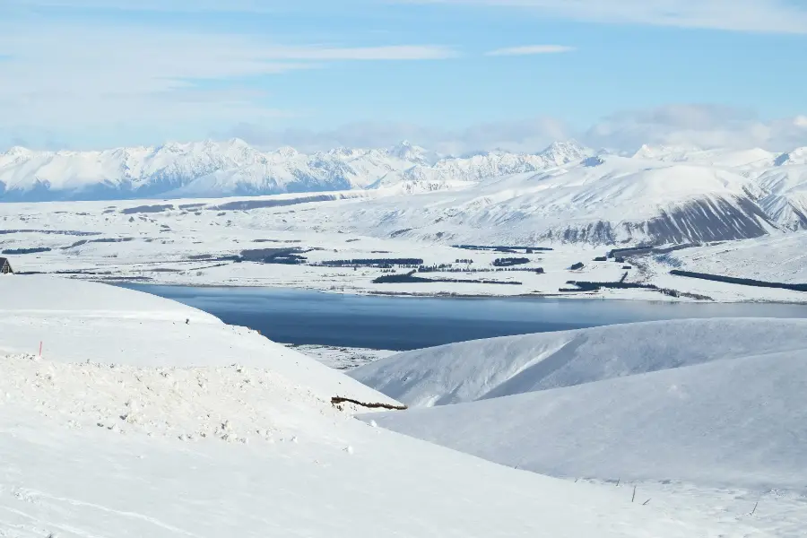 Snow on the slopes of Roundhill ski area, looking down over a winter landscape to Lake Tekapo.