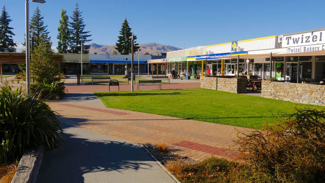 The low shopping centre of Twizel around a lawn and paved paths, under a clear blue sky.