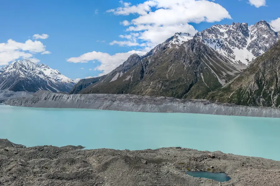 Tasman Lake in its wide glacial valley, grey-blue water scattered with icebergs below bare moraine walls and snowy peaks.