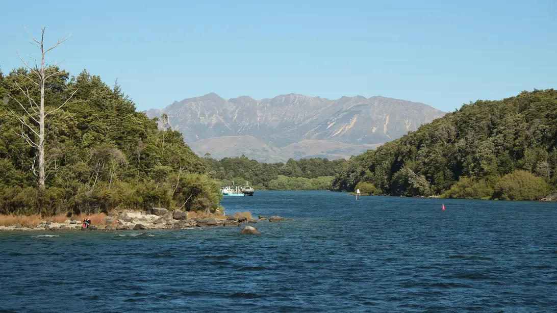 The outlet of Lake Manapouri into the Waiau River towards Pearl Harbour, with bush-covered banks and mountains behind.