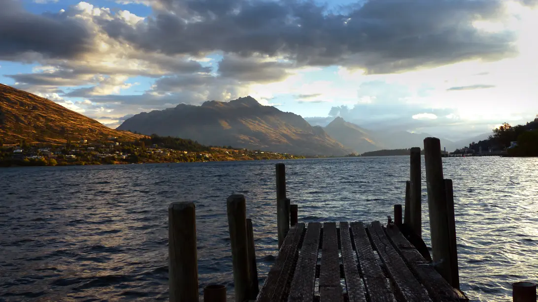 Evening light on the Frankton Arm of Lake Wakatipu, with a wooden jetty in the foreground and mountains across the water.